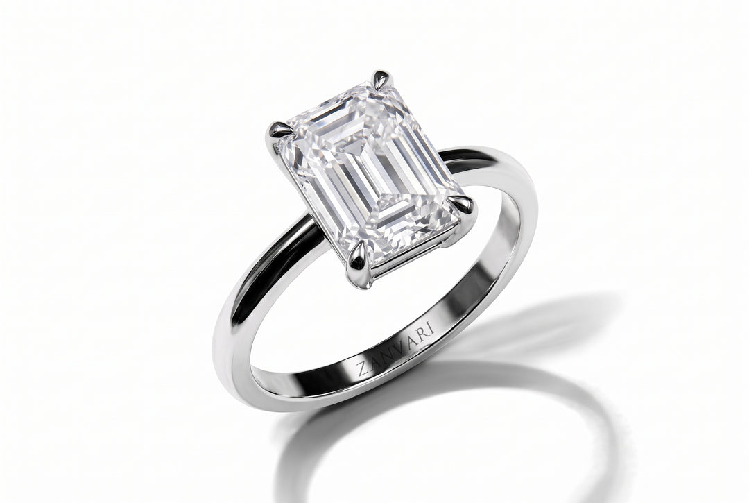 An emerald-cut diamond solitaire ring in a polished silver-colored metal band, shown on a clean white background with a soft shadow.