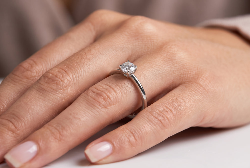 A close-up of a hand wearing a classic solitaire diamond engagement ring on a silver band.