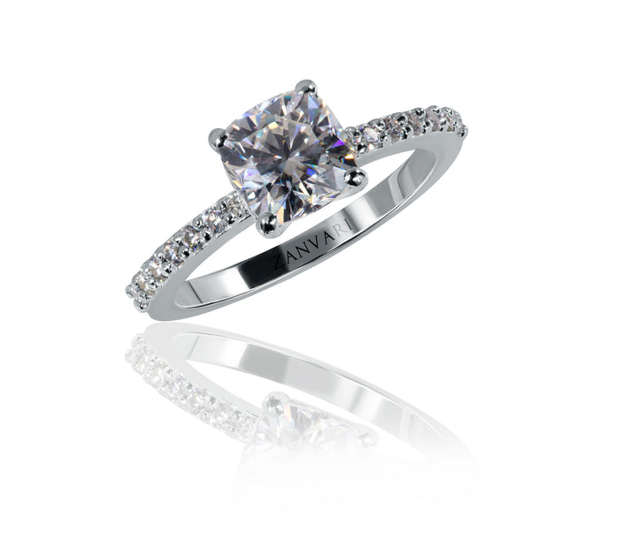 A cushion cut moissanite ring with a white gold rhodium plating and smaller moissanite accents on the band.