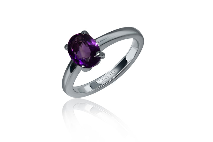 A ring with a oval-cut natural amethyst stone, set in a prong setting on a silver band, with a rhodium plating.