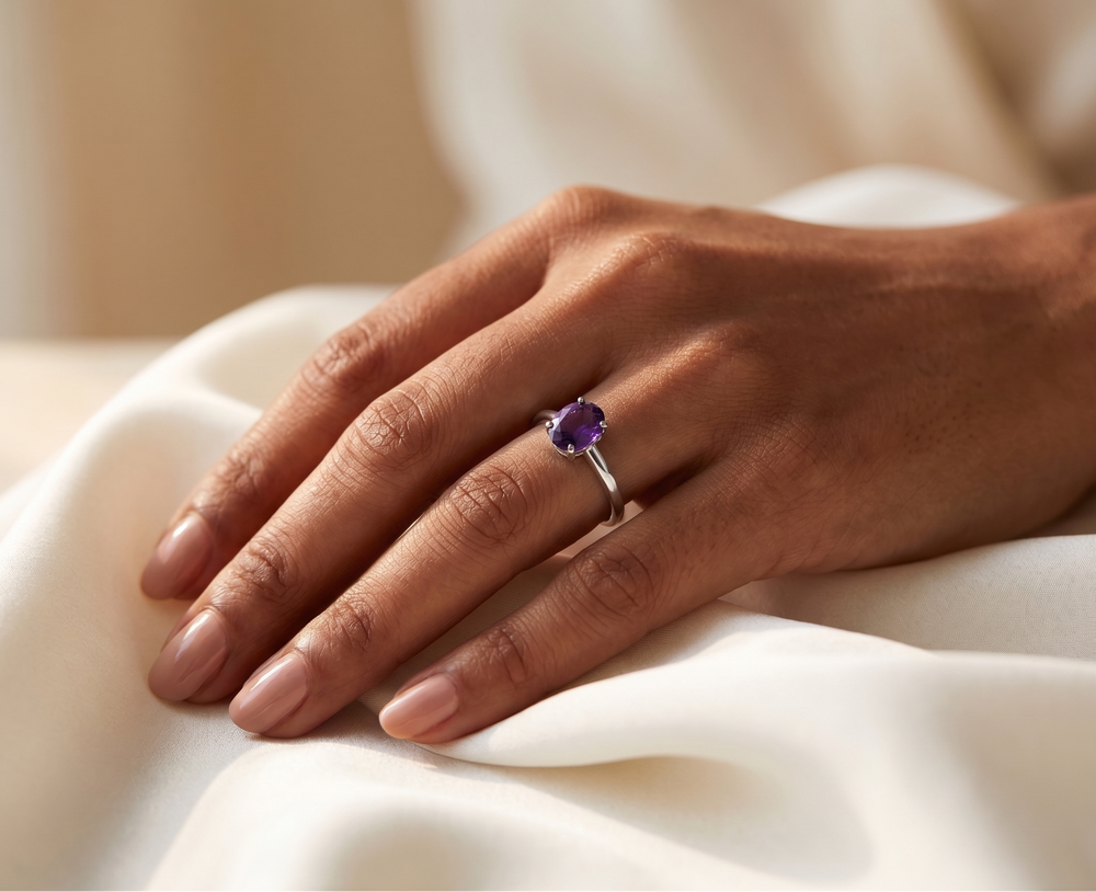 Hand wearing a ring with a amethyst  gemstone on a white fabric background