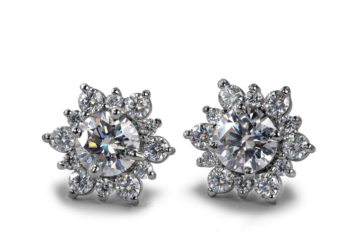 Close-up of a pair of floral halo moissanite stud earrings with central round brilliant stones surrounded by smaller round moissanite petals, set in bright polished metal on a clean white background.