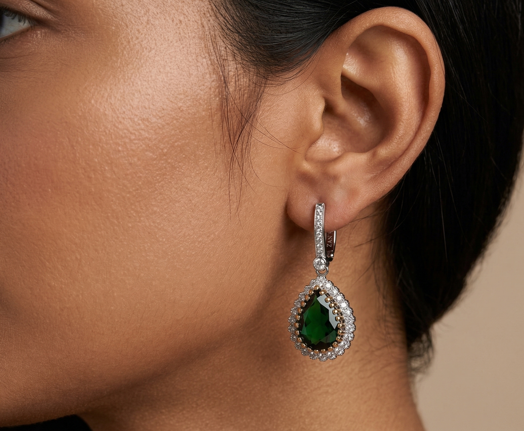 Close-up of a woman wearing a green emerald earring with a beige background