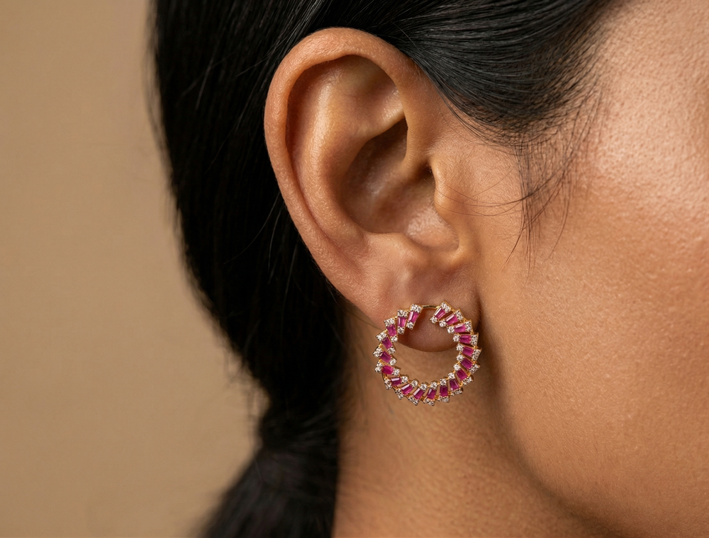 Close-up of an ear wearing a circular earring with pink gemstones against a neutral background