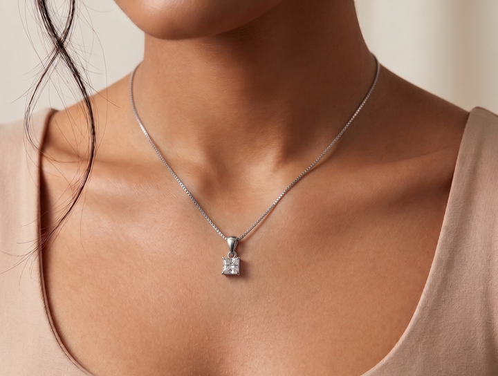 Necklace with a  princess cut moissanite pendant worn by a person in a beige top against a neutral background