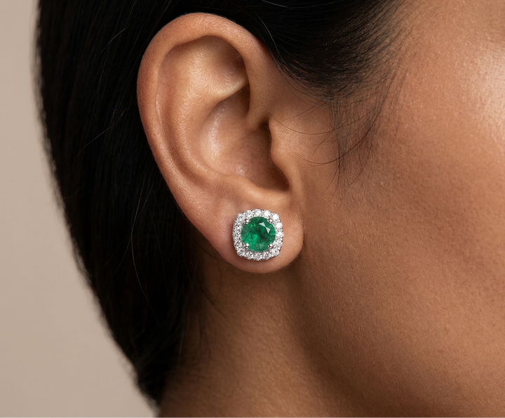 Close-up of an ear wearing a green gemstone earring against a neutral background