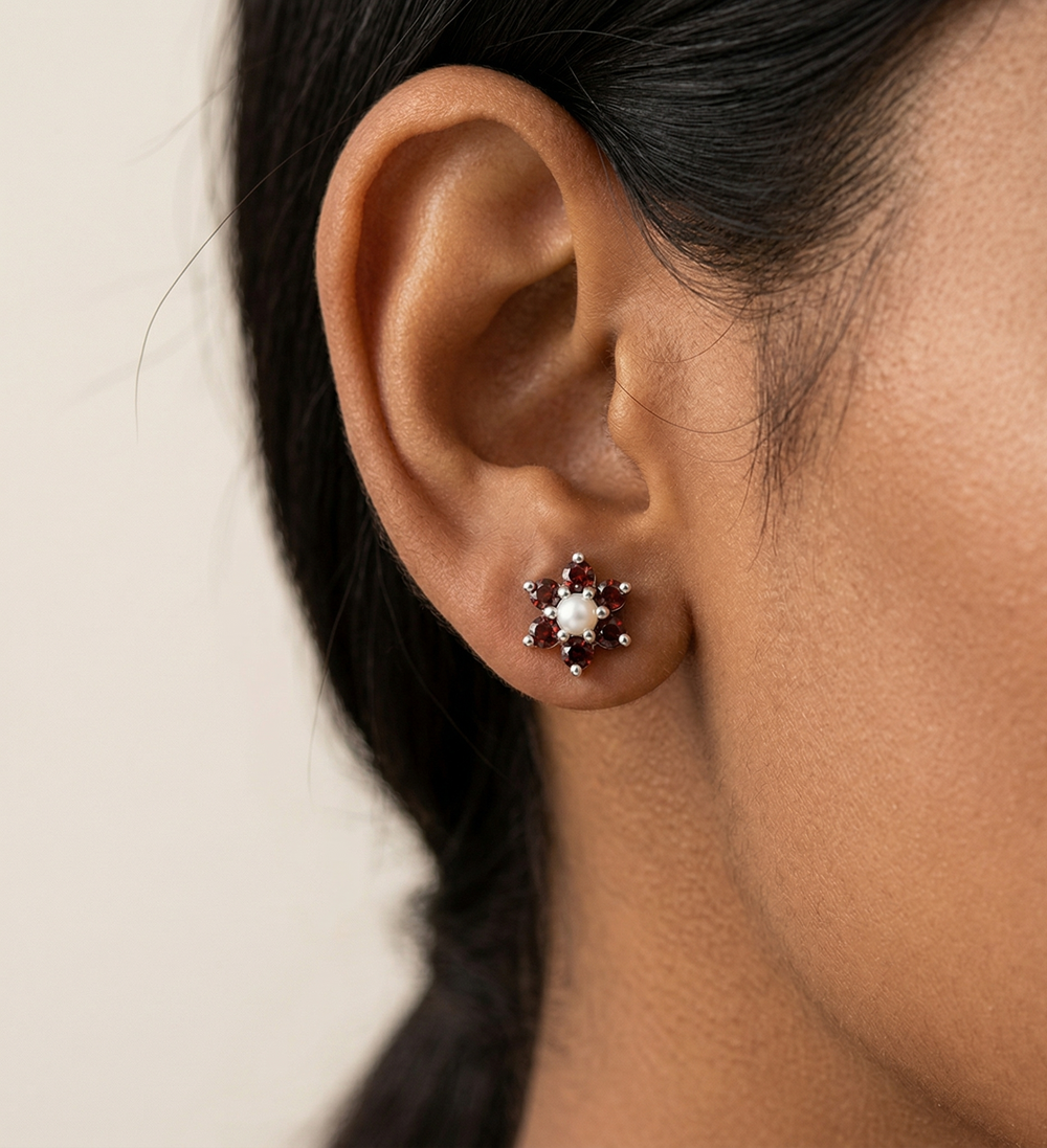 Close-up of an ear wearing a floral garnet earring with a beige background