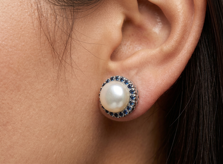 Close-up of an ear wearing a pearl earring with sapphire gemstones.