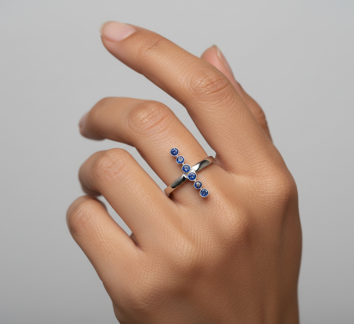 Hand wearing a silver ring with blue gemstones on a gray background
