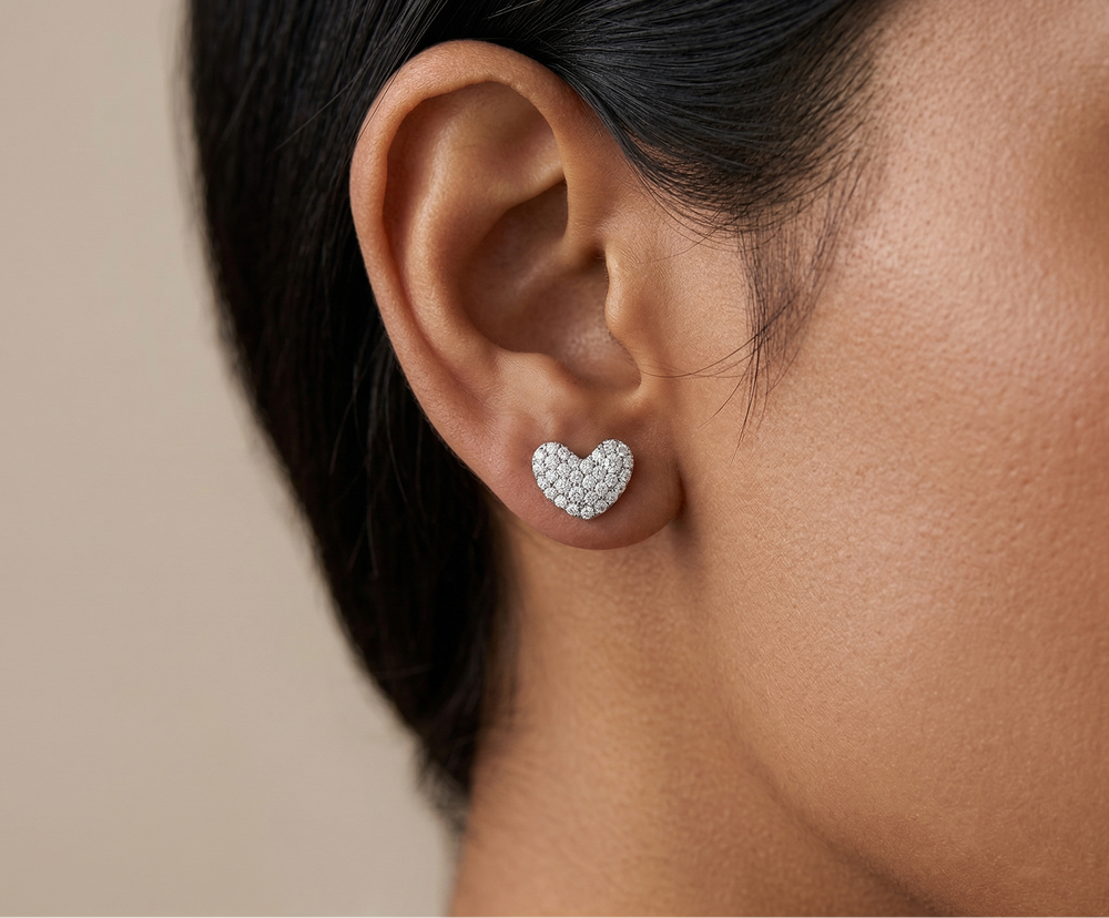 Heart-shaped diamond earrings worn by a person with a neutral background