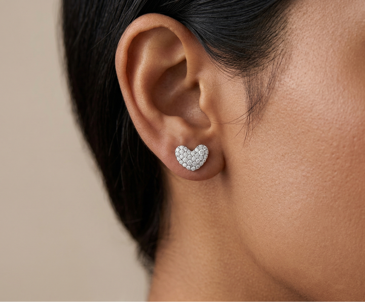 Heart-shaped diamond earrings worn by a person with a neutral background