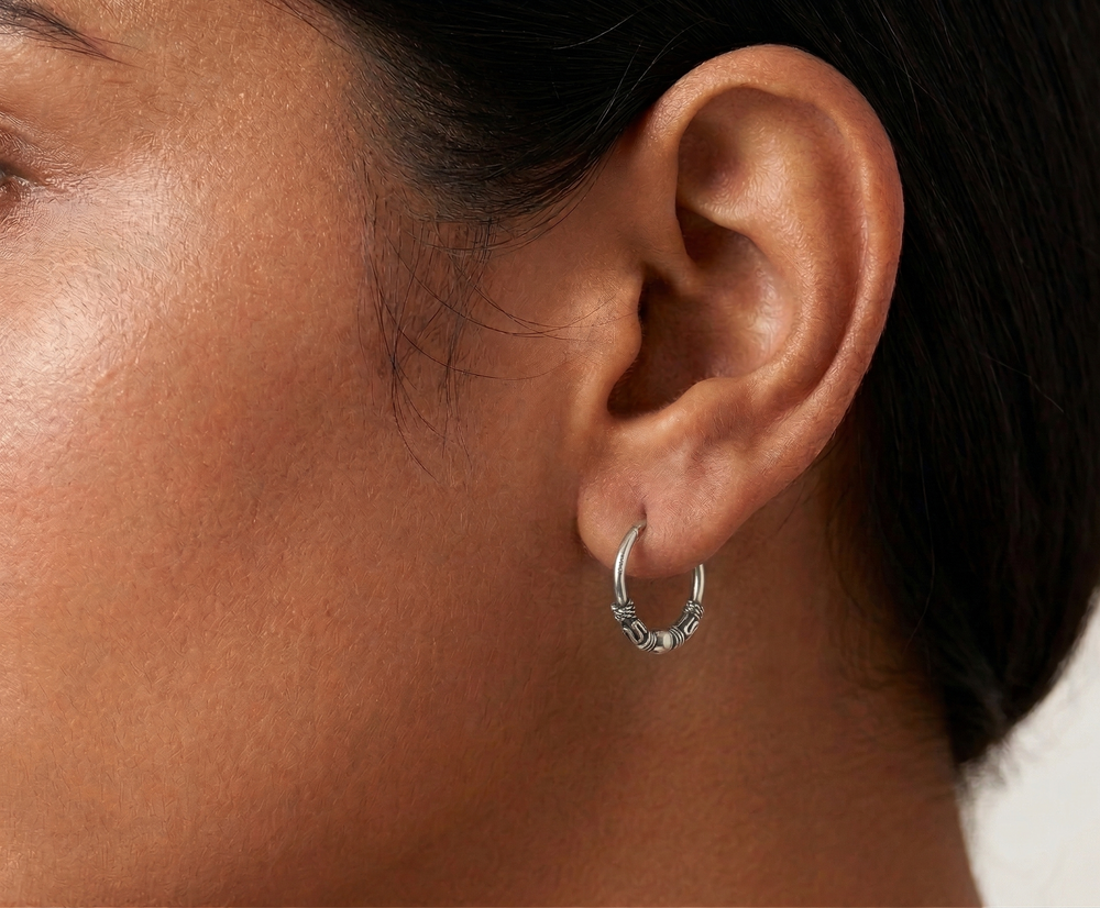 Close-up of an ear wearing a silver hoop earring with a blurred background