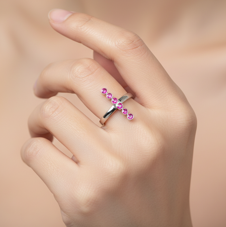 Silver ring with pink gemstones on a hand against a beige background