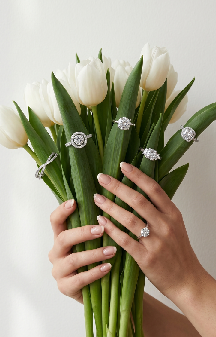 Bouquet of white tulips with moissanite rings on green stems, held by a hand against a light background.