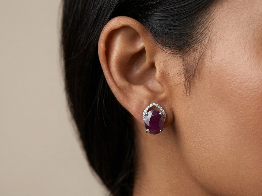 Close-up of a person wearing a silver earring with a red  ruby gemstone against a neutral background