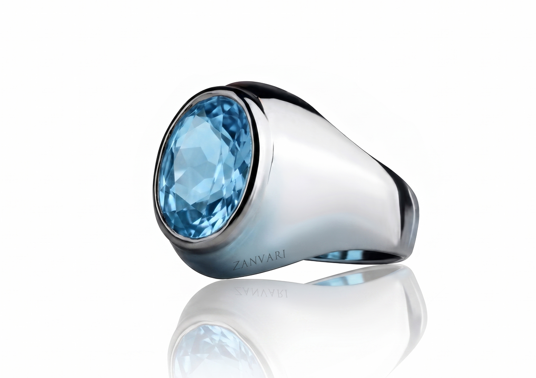 Silver masculine signet ring with an oval-cut light blue Swiss topaz stone set in a sleek bezel, displayed on a reflective white studio background with the logo "ZANVARI".
