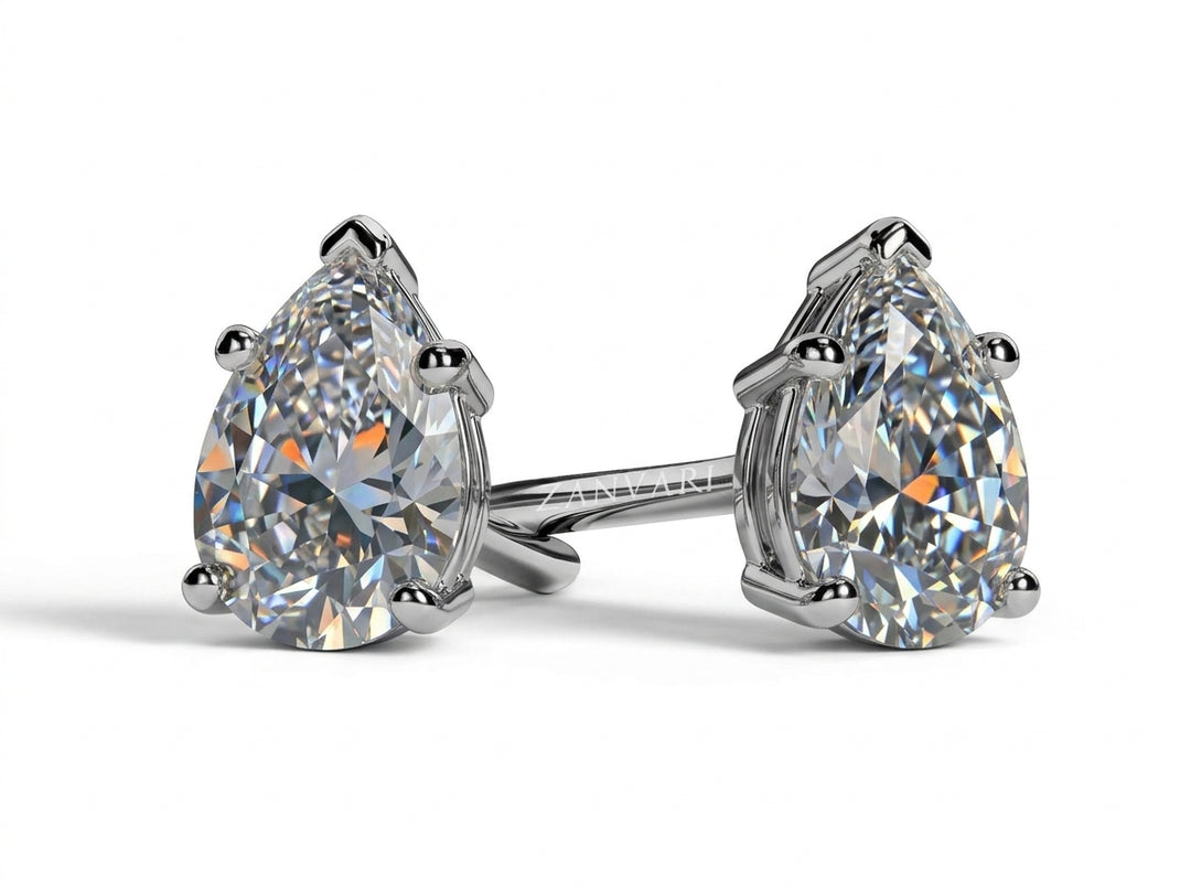 Studio shot of a pair of pear-cut solitaire diamond stud earrings in white gold prong settings against a white background.