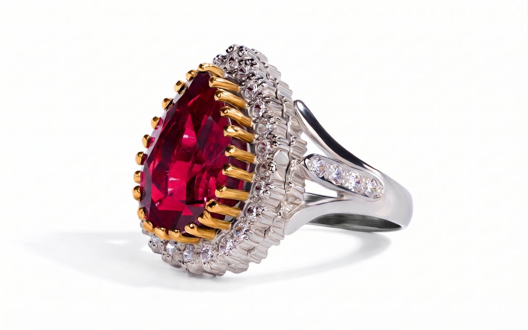 A luxury ring featuring a large pear-cut red gemstone surrounded by gold and silver halos with small clear accent stones, set on a white background.