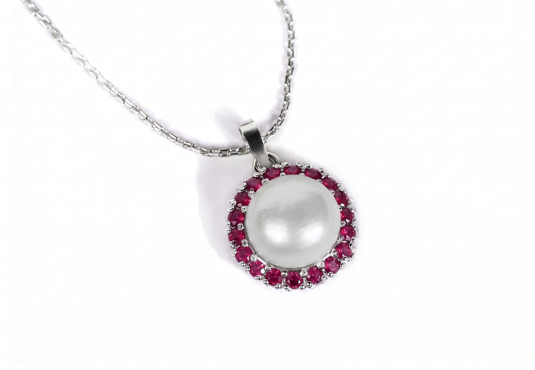 A silver chain necklace with a round pendant featuring a large white pearl surrounded by a halo of small red rubies gemstones, set against a plain white background.