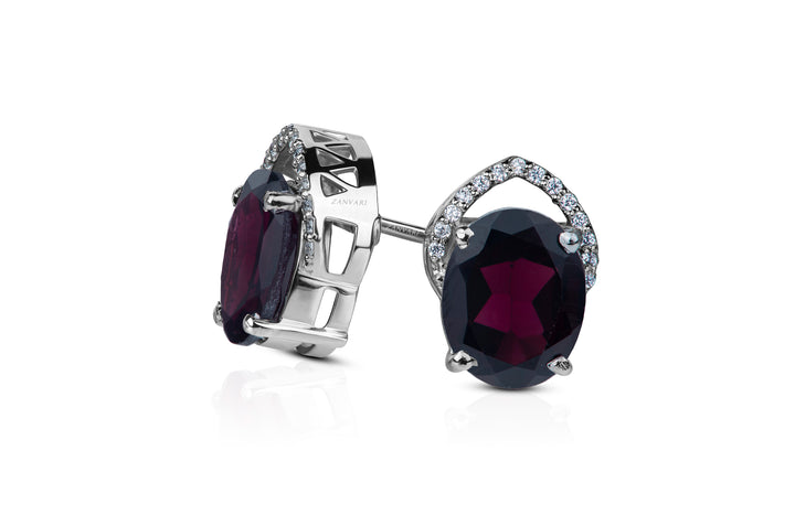 A pair of sterling silver handcrafted stud earrings with deep red garnet centers and surrounding cubic zirconia stones.