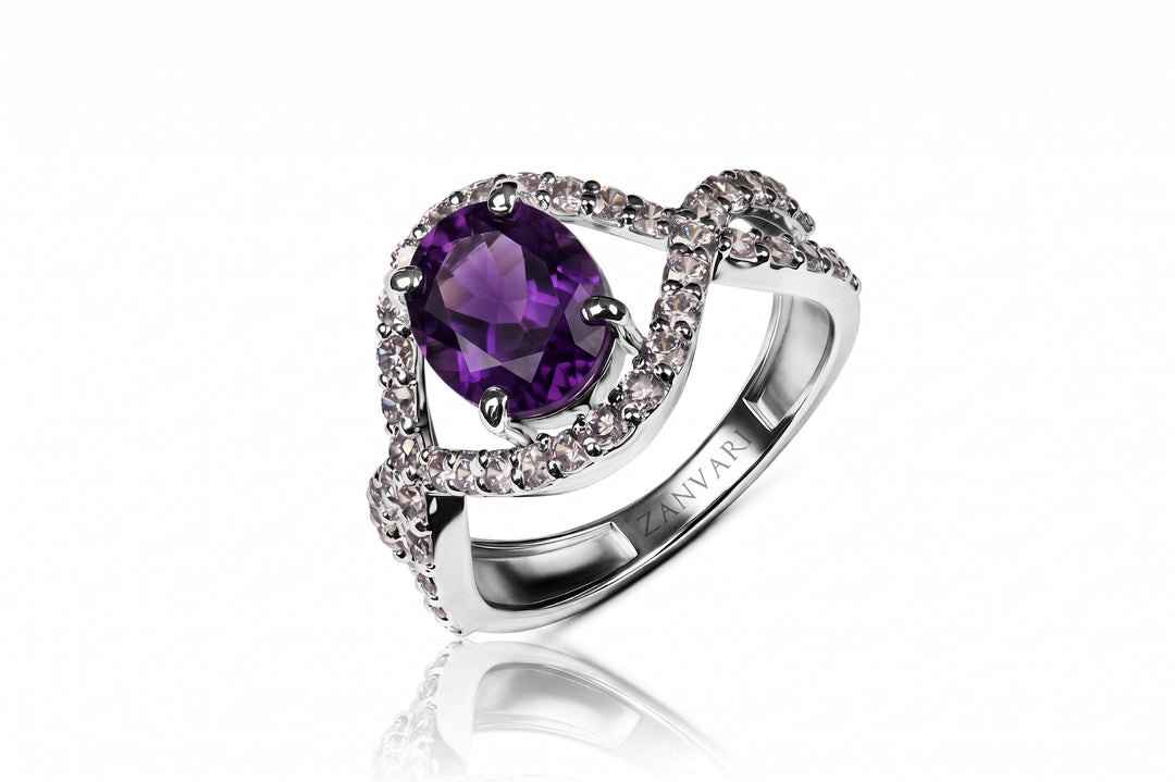 A silver-toned split-shank ring featuring a large oval purple amethyst center stone surrounded by small clear accent stones, shown on a clean white background with a soft reflection below.