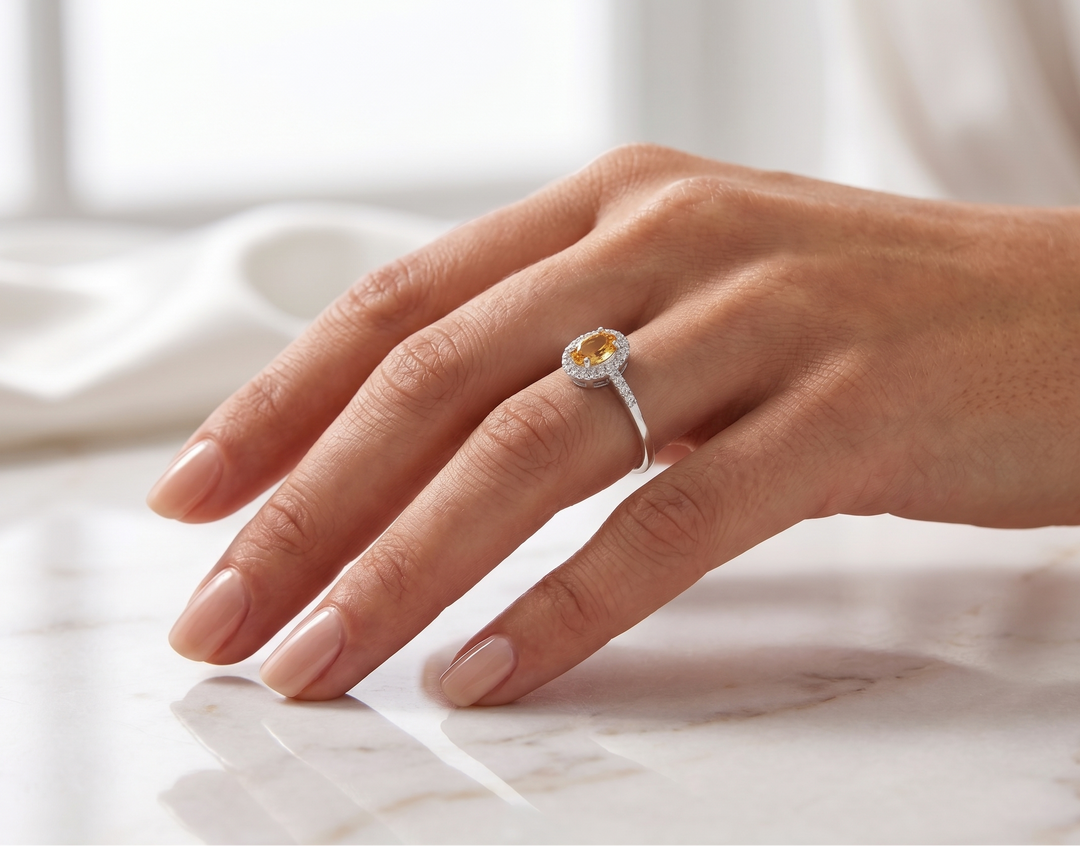 Hand wearing a ring with a yellow  citrine gemstone on a light background