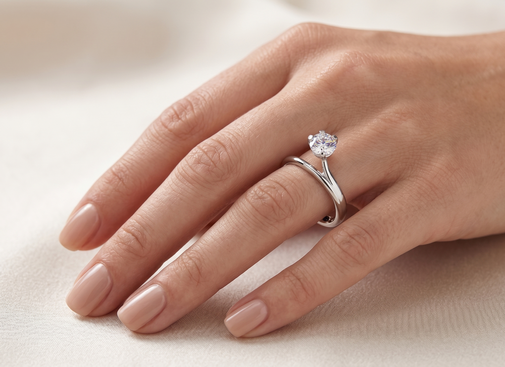 Hand wearing a moissanite proposal ring on a light background