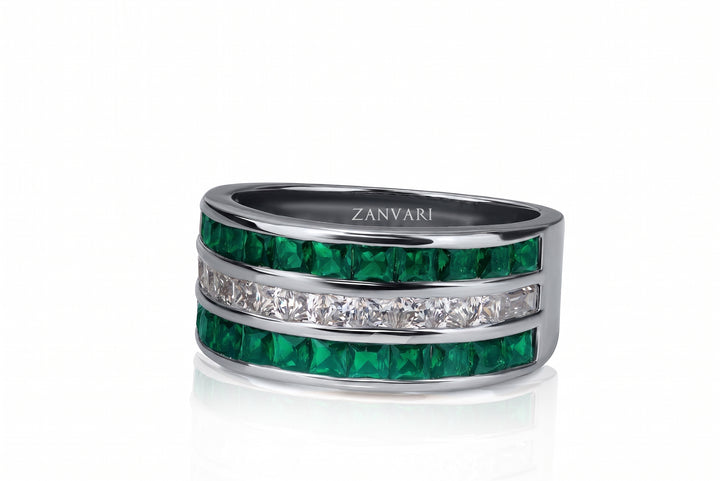 A silver band ring featuring two rows of vibrant green emerald-cut stones and a central row of clear pavé-set stones, with the brand name 'ZANVARI' engraved inside the band, set against a clean white background.