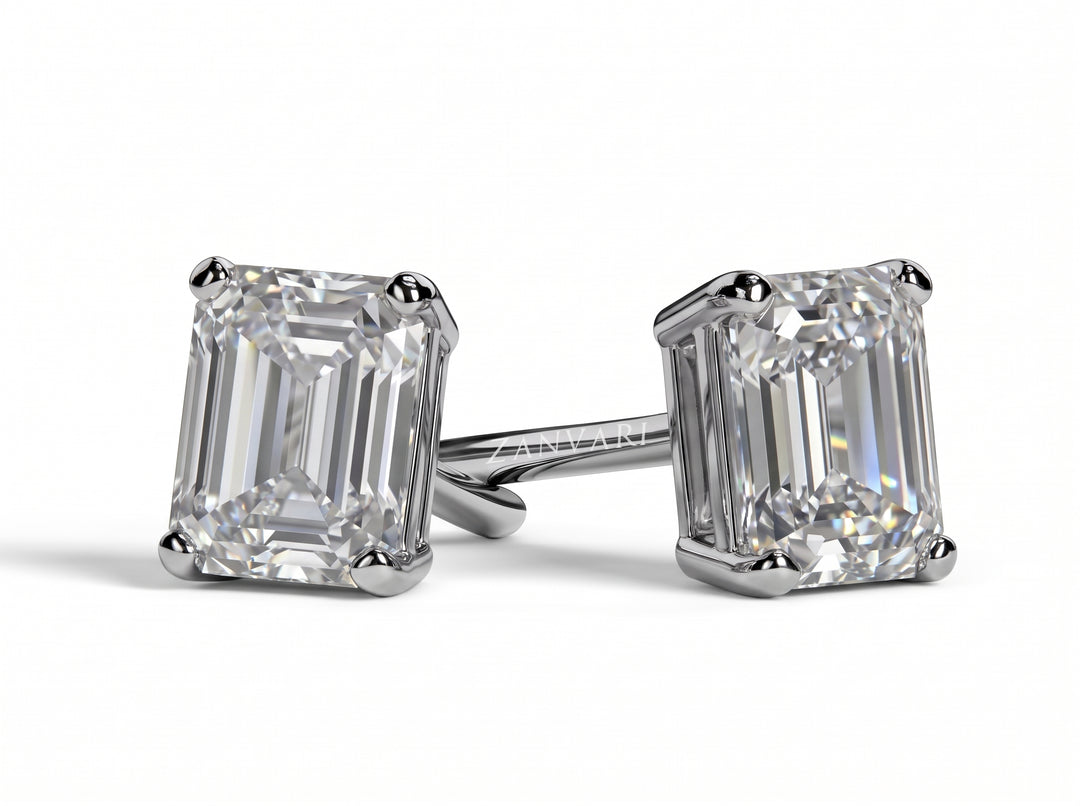 Pair of emerald-cut diamond stud earrings set in four-prong platinum or white gold mounts, resting on a plain white surface with soft shadows.