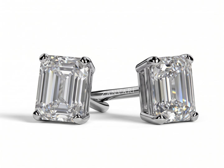 Pair of emerald-cut diamond stud earrings set in four-prong platinum or white gold mounts, resting on a plain white surface with soft shadows.