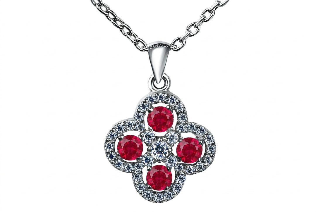 A silver-toned clover-shaped pendant necklace featuring four round red gemstones surrounded by small clear stones, suspended from a silver chain on a white background.