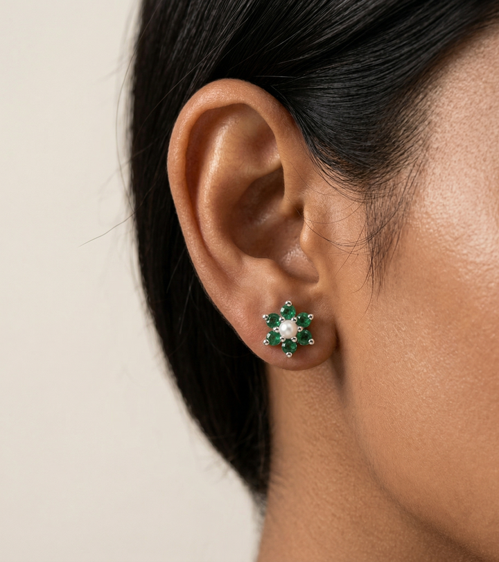 Close-up of an ear wearing a green  emerald floral earring with a neutral background
