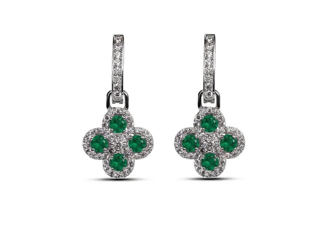 A pair of silver-tone drop earrings featuring a four-petal flower design with round green emeralds surrounded by small clear pavé stones, set against a plain white background.