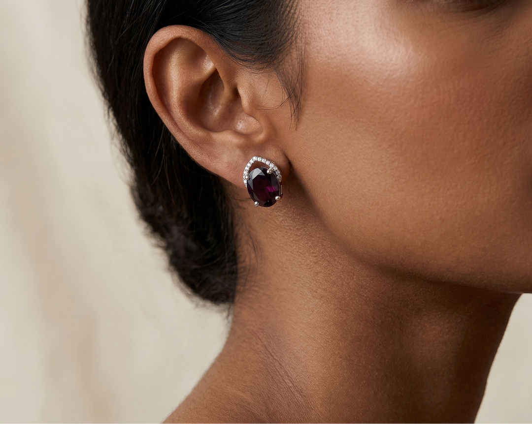 Close-up of a woman wearing a pair of earrings with a red garnet on a neutral background