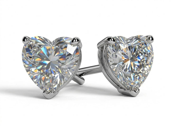 A pair of heart-shaped moissanite stud earrings in a silver four-prong setting, shown on a clean white background.