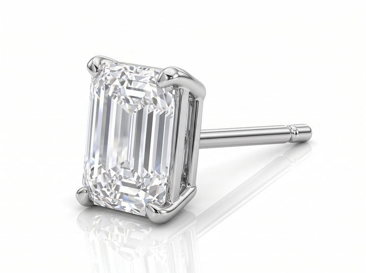 An emerald-cut diamond stud earring in a silver-colored metal setting, shown on a clean white background with a soft reflection underneath.