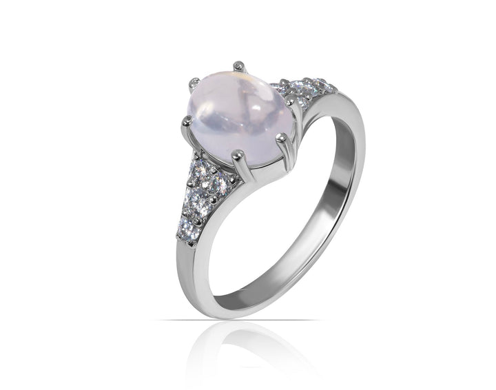 A silver-toned ring featuring a large oval moonstone pale pinkish-white center stone, accented by small clear stones along the shoulders, shown on a white background with a soft reflection.