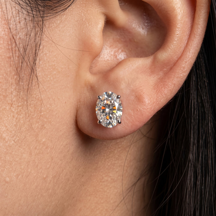 Macro shot of a woman wearing a modest oval-cut moissanite stud earring set in four white-metal prongs on her earlobe.