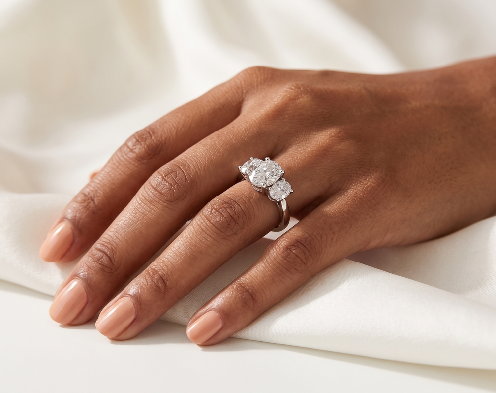 Hand wearing a moissanite oval cut silver ring on a white fabric background