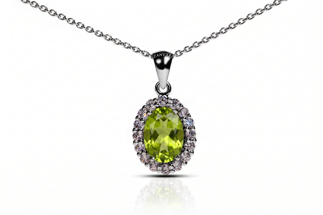 An oval pendant necklace featuring a vibrant green peridot stone surrounded by a halo of small clear stones, set in a silver-toned metal and suspended from a matching silver chain on a white background.