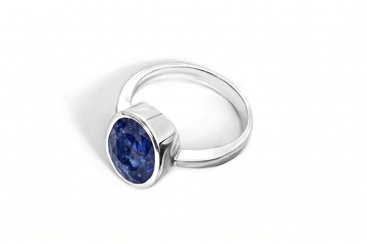 A silver ring featuring an oval-cut deep blue gemstone in a bezel setting, shown on a clean white background.