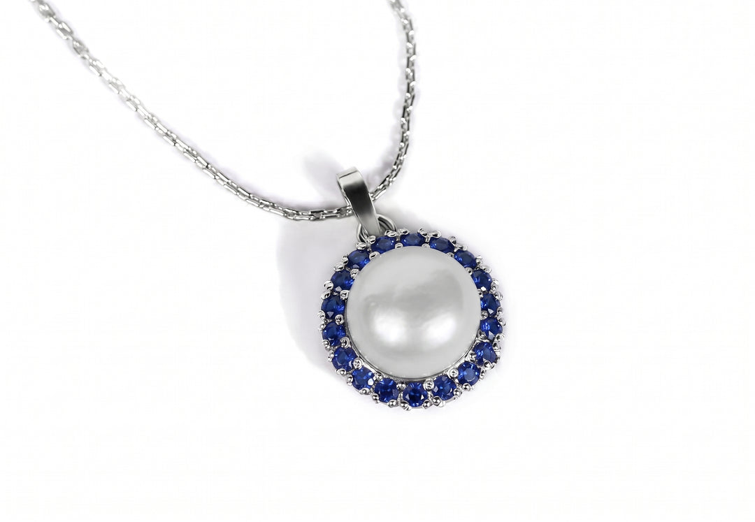 A silver chain necklace with a round pendant featuring a large white pearl surrounded by a halo of small blue sapphiregemstones, set against a plain white background.