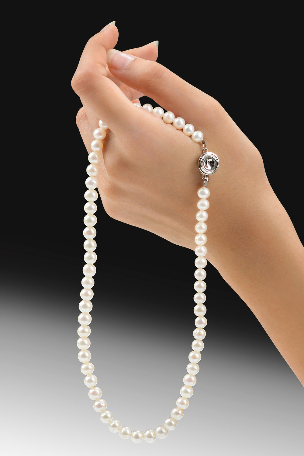 Model hand gracefully holds a string of white pearls with a silver clasp against a black background, perfect gift extract from the nature