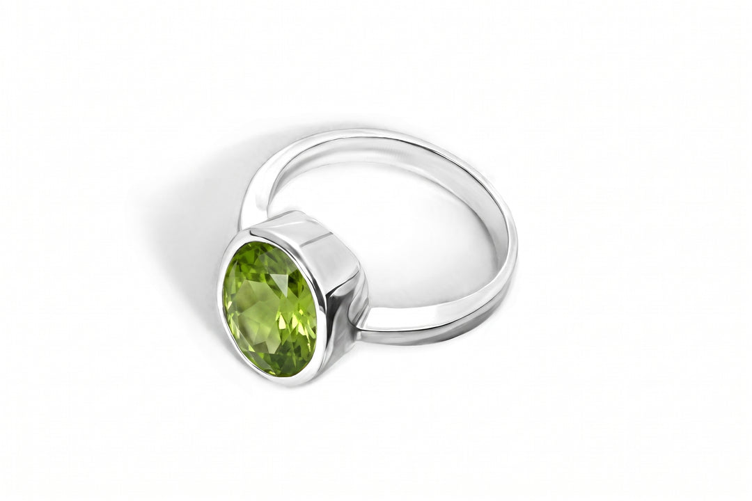 A silver ring featuring a faceted green peridot gemstone in a bezel setting, shown on a clean white background.