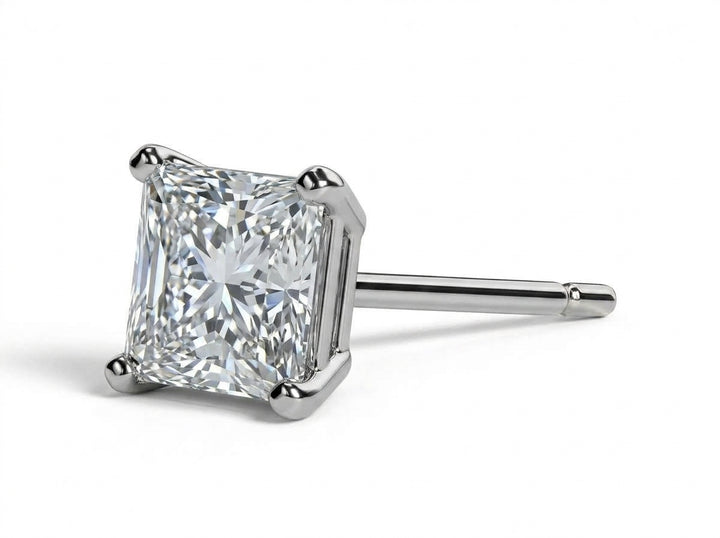 Close-up studio shot of a 1-carat princess-cut diamond stud earring mounted in a 4-prong white gold basket setting, viewed in profile against a clean white background.