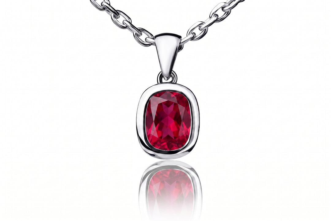 A silver pendant necklace featuring a cushion-cut, faceted deep red ruby gemstone, shown on a clean white background with a soft reflection below.