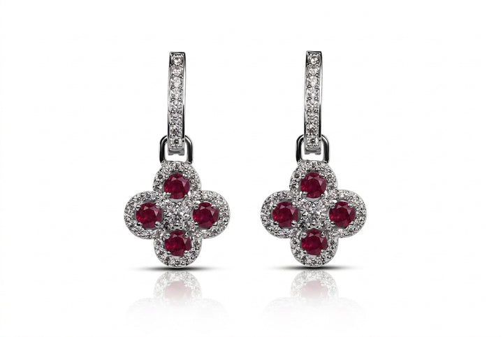 A pair of silver-tone dangle earrings featuring a four-petal flower design set with round red gemstones and surrounded by small clear pavé stones, shown on a white background with a soft reflection.