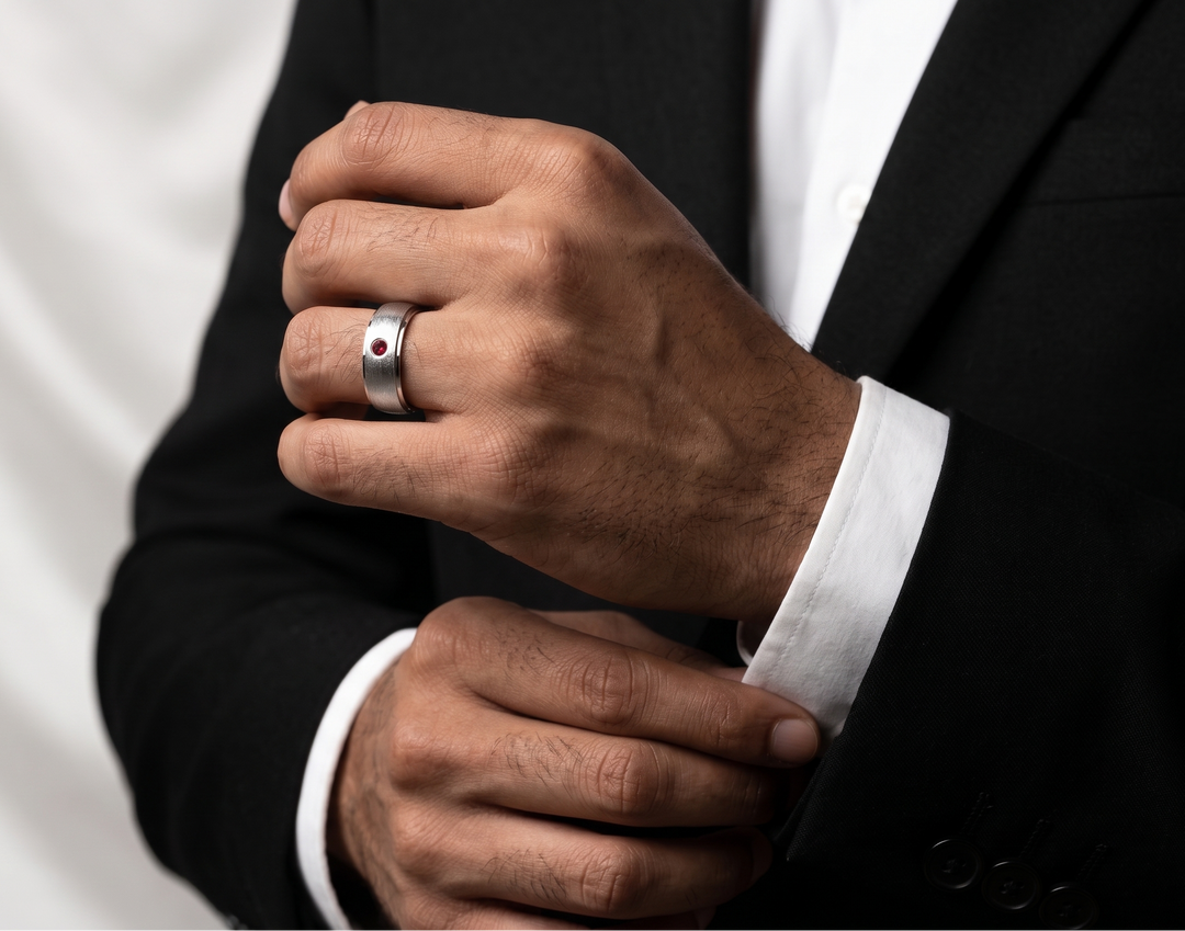 Close-up of a person wearing a black suit with a white shirt and a silver ring on a plain background.