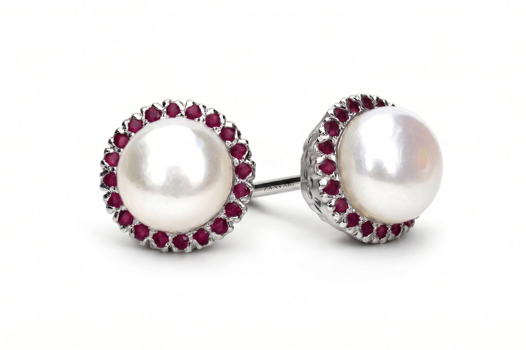 A pair of round stud earrings featuring large white pearls surrounded by a halo of small red gemstones in a silver-toned setting, shown on a plain white background.