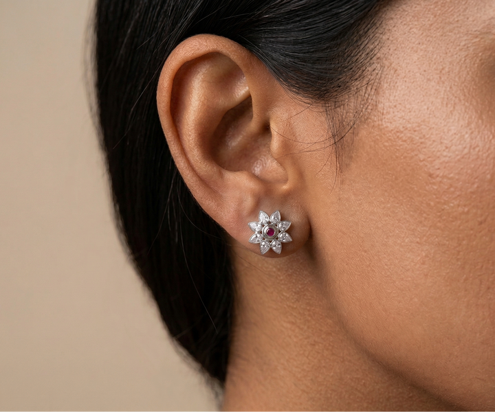 Close-up of an ear wearing a floral earring with gemstones on a neutral background